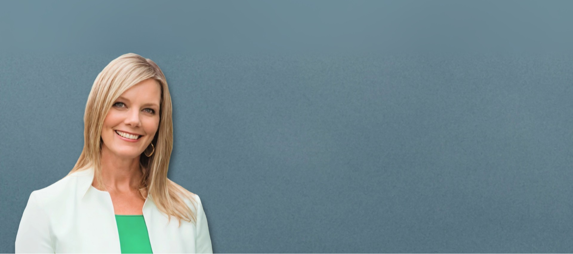 Woman in a white blazer and green top standing against a plain blue background